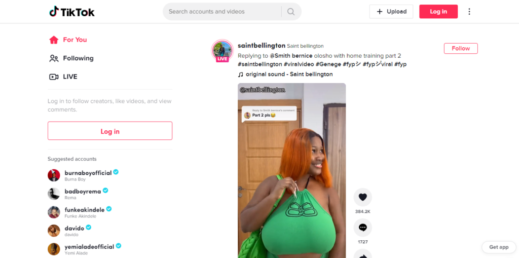 TikTok Make Your Day - CyberNaira A screenshot of the TikTok desktop website interface. The left sidebar displays navigation links for "For You," "Following," and "LIVE," alongside a list of suggested accounts including Burna Boy, Rema, and Funke Akindele. The center feed shows a video post by creator "saintbellington" featuring a woman with bright orange hair wearing a green top. Interaction icons for likes, comments, and shares are visible on the right side of the video. The top header includes the TikTok logo, a search bar, and buttons to "Upload" and "Log in."