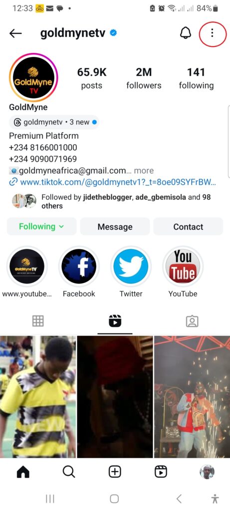 Goldmyetv Instagram profile page - CyberNaira A mobile screenshot of the verified Instagram profile page for "goldmynetv." The account is a verified "Premium Platform" with 2 million followers, 65.9K posts, and 141 following. The profile includes contact phone numbers, an email address, and a link to a TikTok profile. Below the bio, buttons for "Following," "Message," and "Contact" are visible, along with circular story highlights for YouTube, Facebook, Twitter, and TikTok. A red circle in the top right corner highlights the three-dot menu icon.